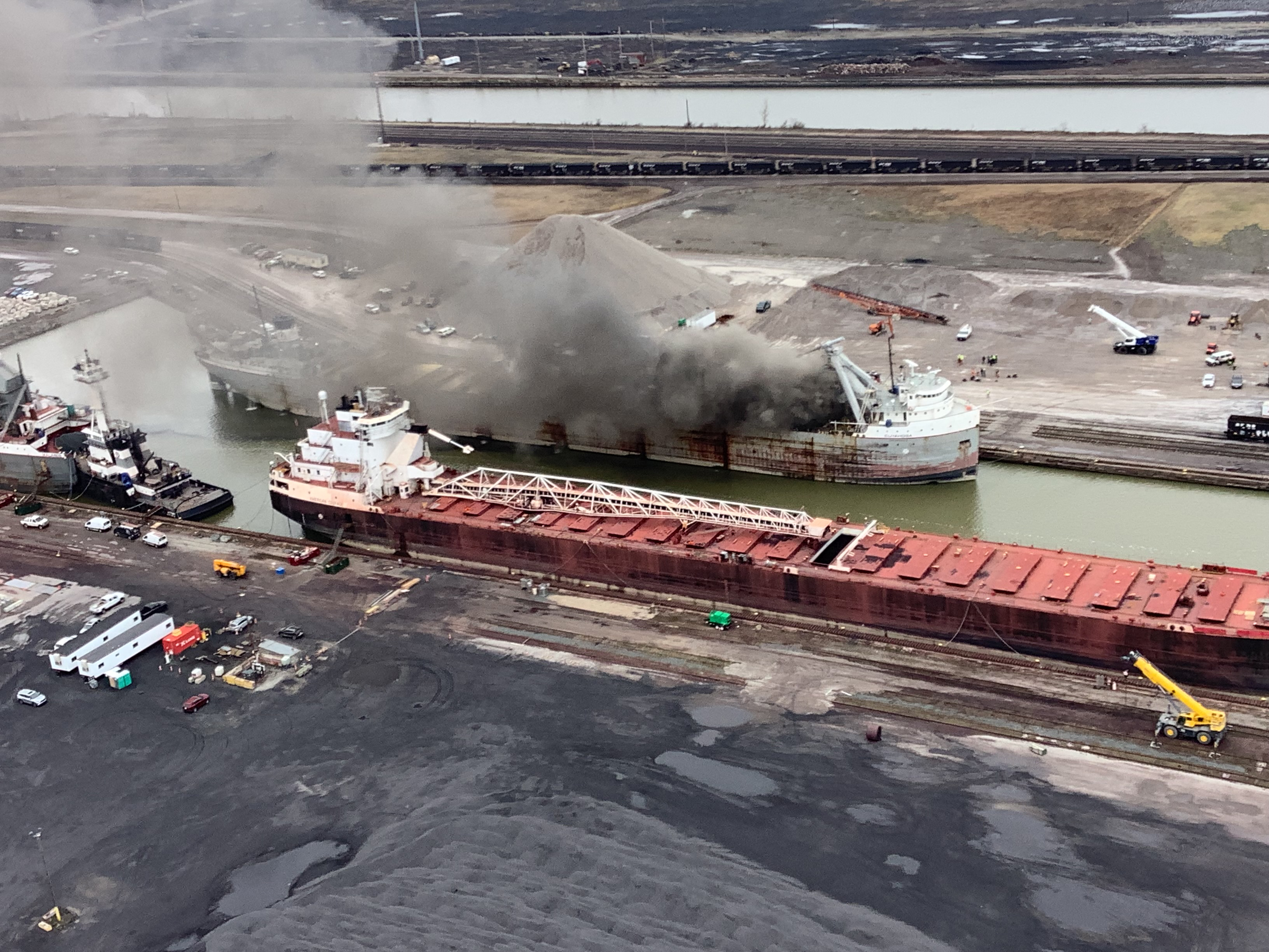 Large bulk freighter on fire while docked in a port.
