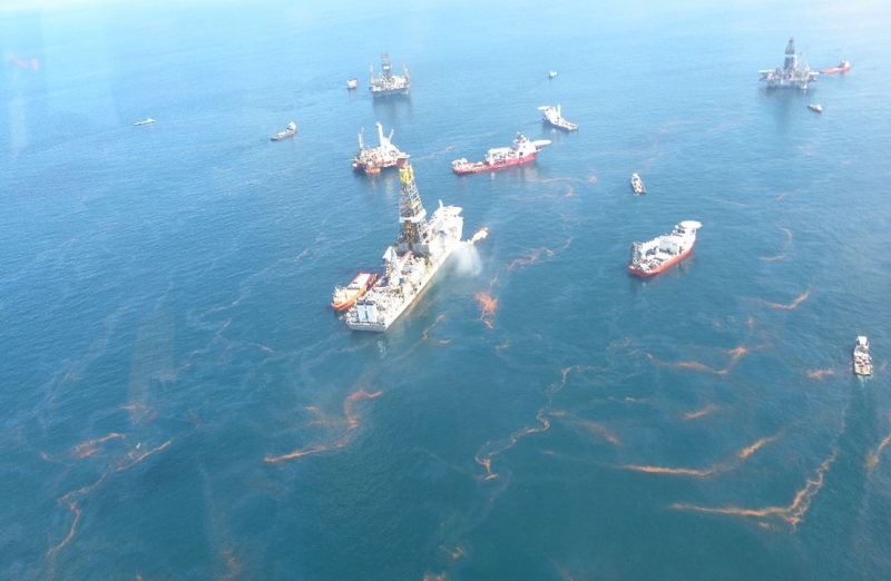 An overflight image showing a drilling rig with oil around it.