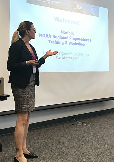 A woman standing in front of a projector screen that reads "Norfolk NOAA Regional Preparedness Workshop and Training."