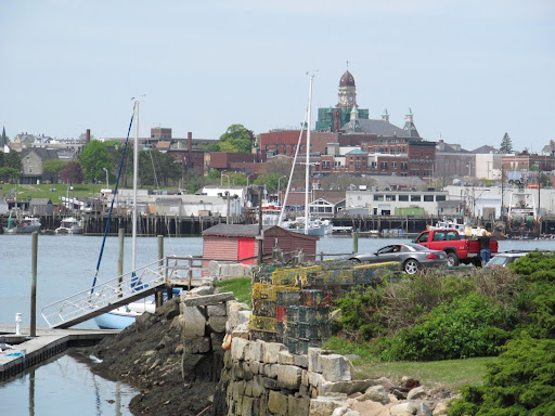 Harbor scene with sailboats, lobster traps, a red truck, and a cityscape featuring a domed clock tower.