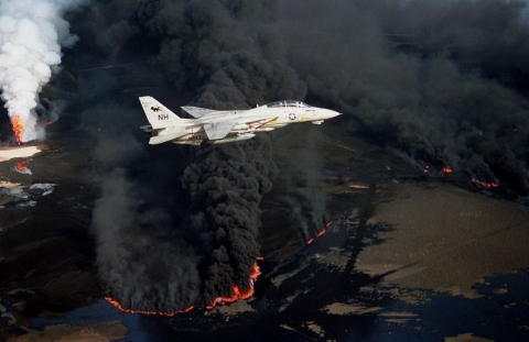 A jet plane flying in front of a large, black plume of smoke.