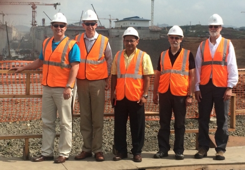 A group of five people standing in orange vests and hard hats in front of a construction site.