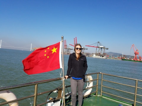 A woman next to a Chinese flag with water and an industrial shoreline in the background. 
