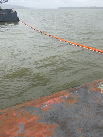 Pollution boom containing a red substance in water.