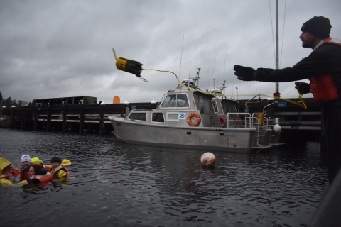 A man tosses an object toward a group of people in water. 