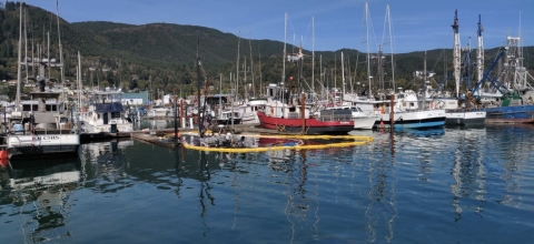 The top of a boat visible above the water surrounded by pollution boom at a marina.