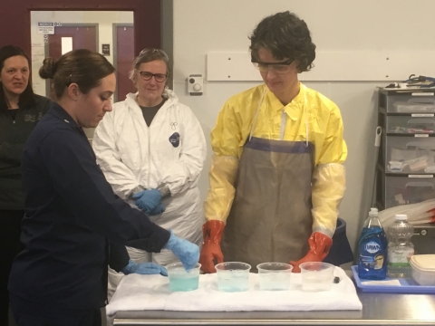 People standing around a table with four containers of liquid in it.