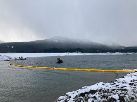 A spill boom deployed across a lake with mountains in the distance.