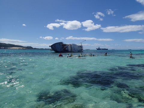 A group of people on paddleboards with an overturned, grounded vessel behind them.