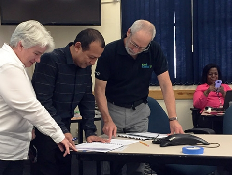 Three people standing around a table looking over documents. 