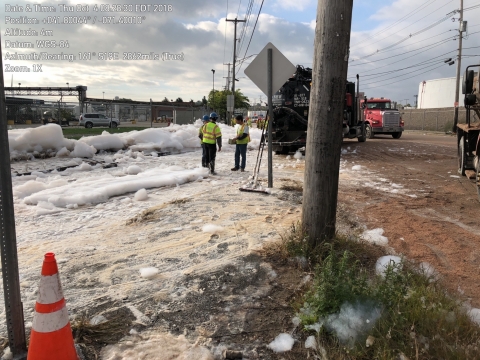 Three people walking through firefighting foam on the ground.