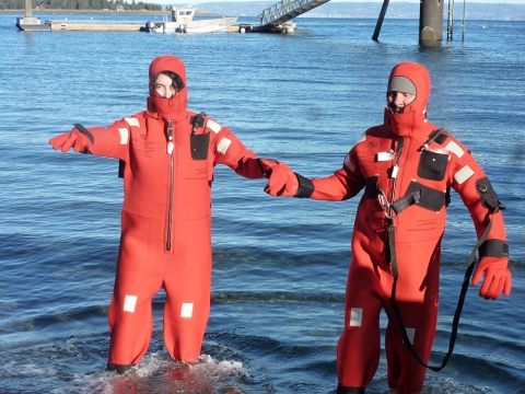 Two people in orange wet suits wade through the water. 