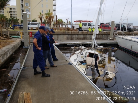 Three people on a dock looking at a sunken vessel.