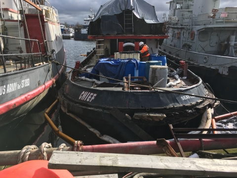 A person working on a vessel surrounded by pollution boom. 
