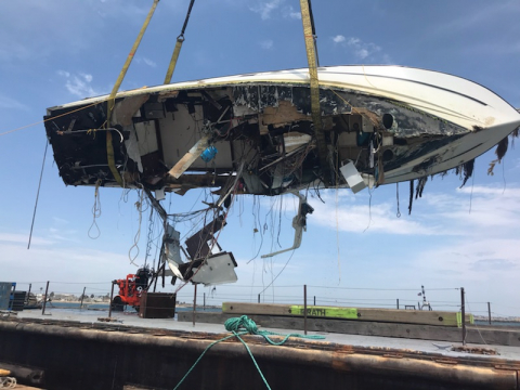 A damaged boat being raised by a crane.