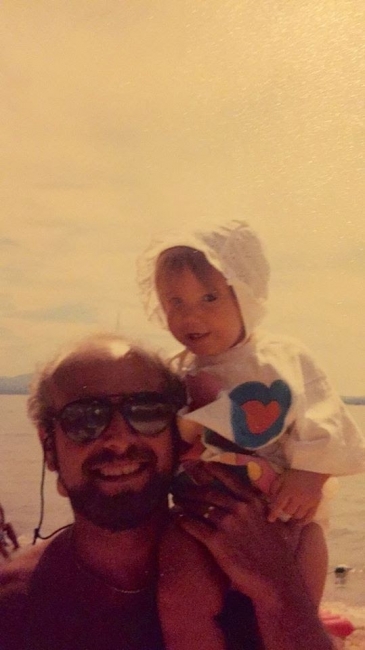 A child on a man's shoulders with a body of water in the background.