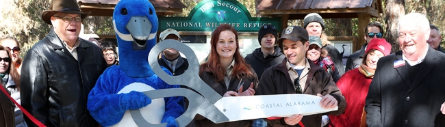 A group of people and a person in a bird mascot costume hold a giant pair of scissors and pose for a photo. 