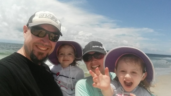 From left, a man, a child, a woman, and another child posing for a photo on a beach.