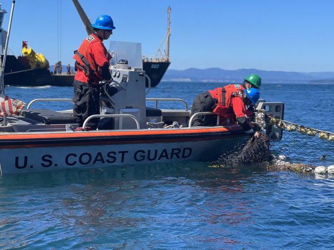 A person in a life vest reaching over a vessel to grab a fishing net.