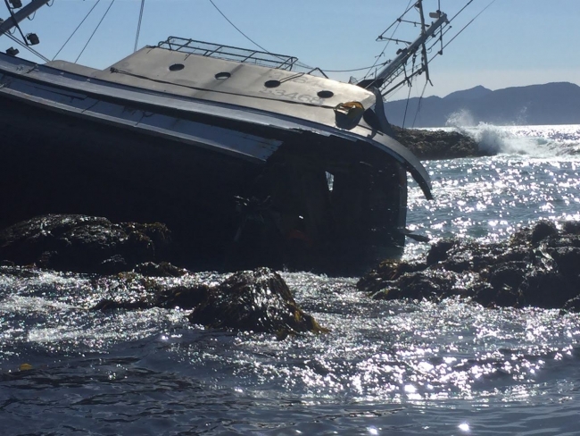 A vessel on its side on a rocky shoreline.