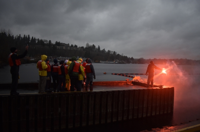A man holding a flare at the end of a dock with a group of people on it. 