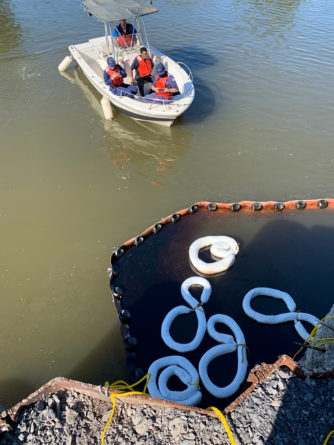 A boat with of people on it moving toward an area of oil in the water confined by pollution boom.