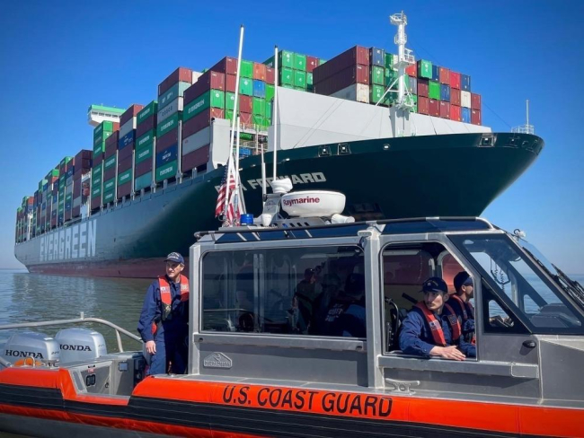 A smaller boat with several people on it and a containership in the background.