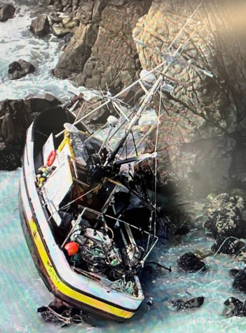 Fishing vessel grounded up against a steep, rocky, coastal terrain.