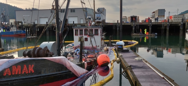 A boat surrounded by pollution boom sinking at a dock. 
