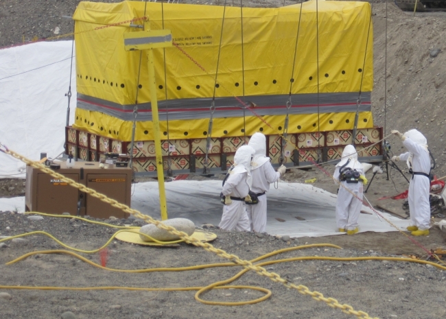 People in Hazmat suits preparing a tarp covered object for removal. 