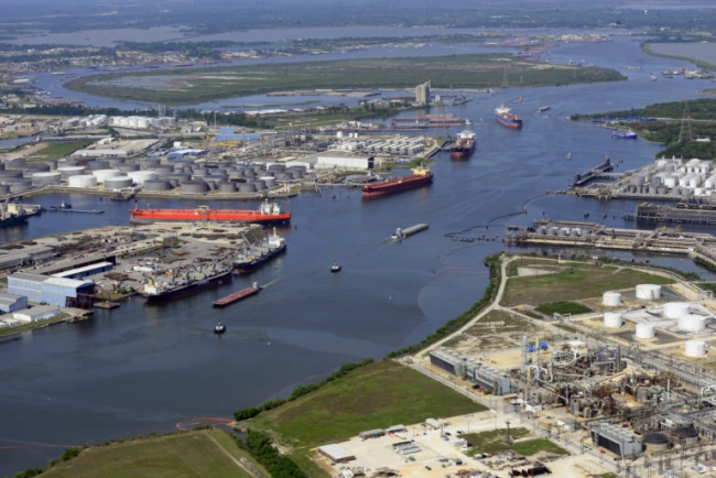 An aerial view of an industrial shoreline with several vessels in a river/canal and polllution boom visible along the shoreline.