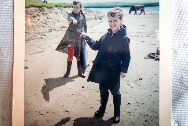 Two kids on a beach holding a fish. 