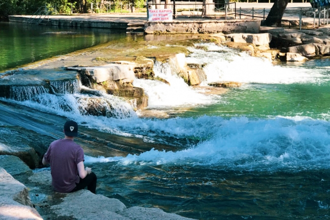 A man sitting on a rock with his feet in a river.