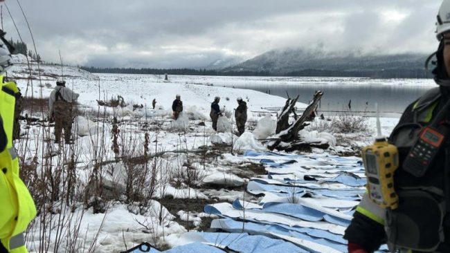 A response team laying down sorbent pads on a snowy shoreline.