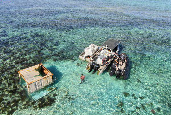 People aboard three small vessels collect materials left behind on a reef after a vessel was stranded.