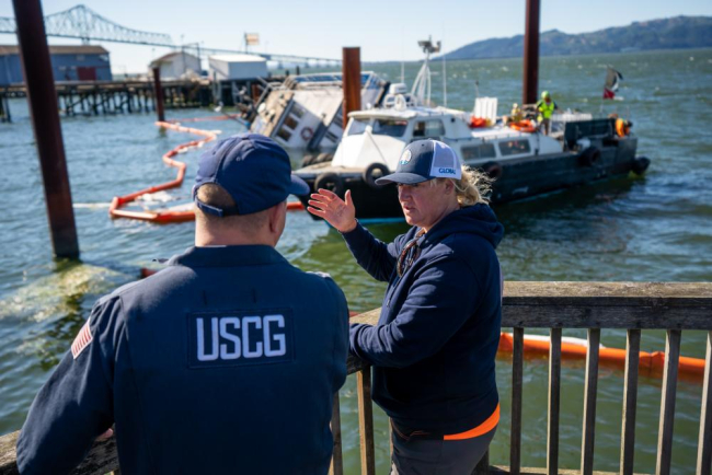Two people in uniform on a dock with a vessel in the background.