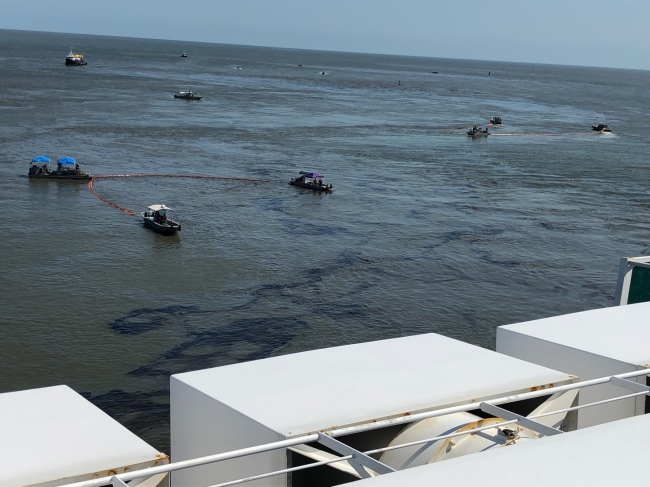 A view of a dark product in the water with several boats and skimmers around it. 