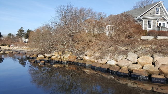  House at water's edge with oiled boulders.