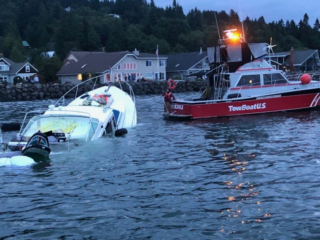 A vessel towing a partially sunken vessel through water.