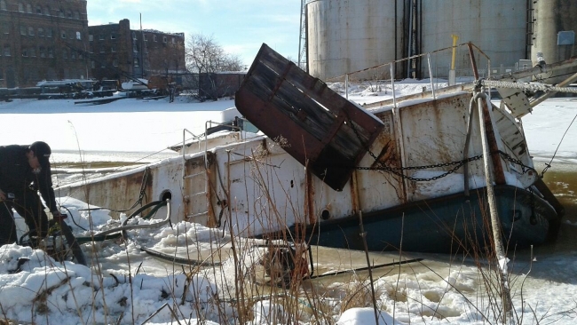 A person standing next to a sunken vessel surrounded by ice and snow. 