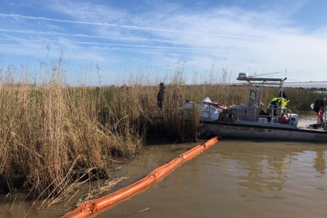 A boat in water with pollution boom around a marsh. 