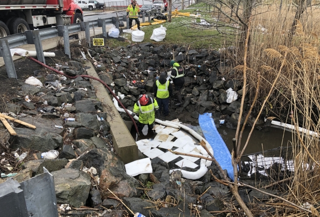 People in response gear applying pollution sorbent to a creek area.