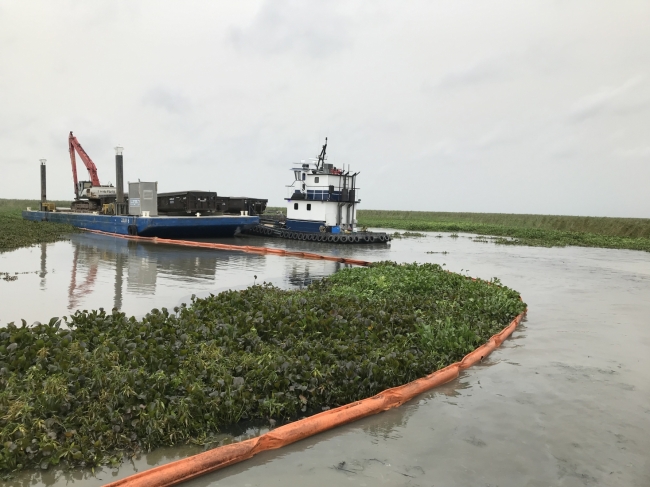 A boat and pollution boom in a marsh area. 