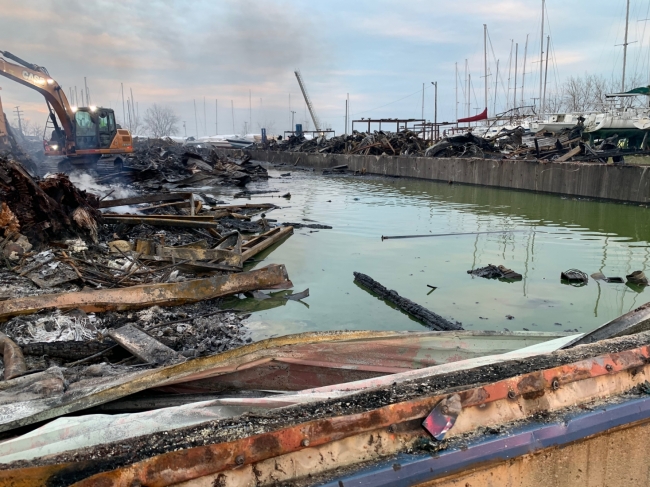 Debris from a burned building next to a ditch of green liquid. 