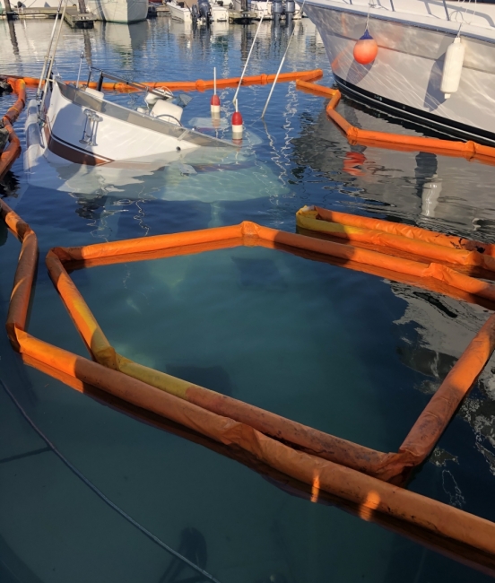 A sunken vessel surrounded by pollution boom in a marina.