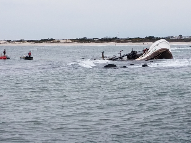 A vessel run aground and sinking with people on a boat nearby.