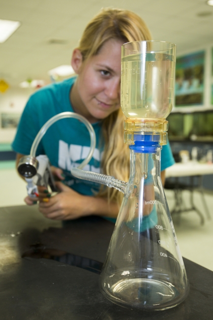 A woman in a lab looking into a flask with a scientific instrument attached to it. 