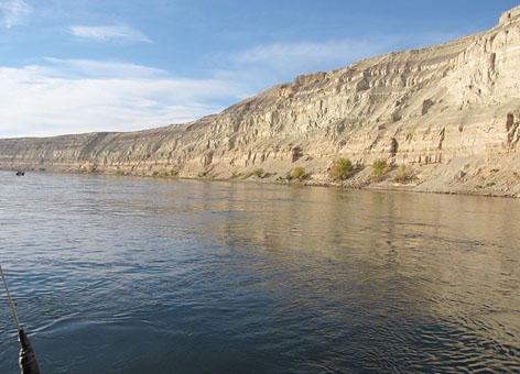 A river with a rocky hillside on the far shoreline. 