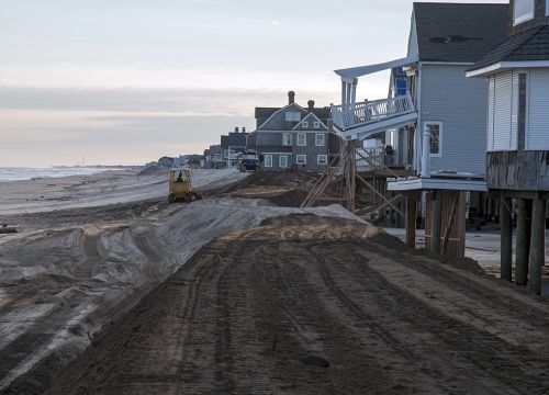 Construction machinery on a beach near damaged houses. 