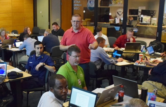 A man standing among a work area with people at computers.